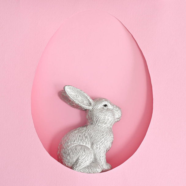 Easter ceramic bunny rabbit in egg shape frame on pastel pink background. Creative spring holidays concept - 写真・画像