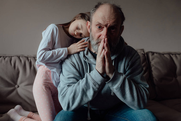 Σταματήστε τον πόλεμο. Ουκρανός ανήσυχος μεσήλικας άντρας που υποστηρίζει ένα φοβισμένο εγγόνι. Δυστυχισμένος ώριμος παππούς με κοριτσάκι στο σπίτι. Προσευχήσου για την Ουκρανία. Είμαστε με την Ουκρανία. - Φωτογραφία, εικόνα