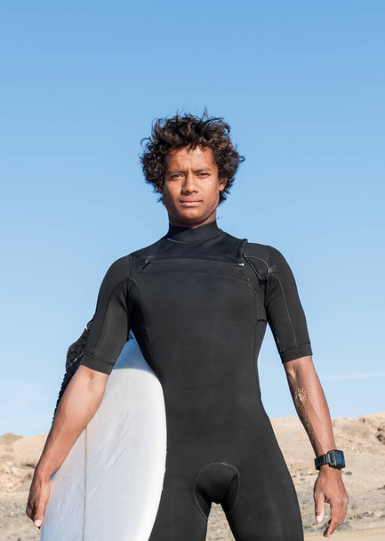 Mladý africký malagasy atletický surfař portrét držení surfovací prkno na sobě černé neoprén - Fotografie, Obrázek