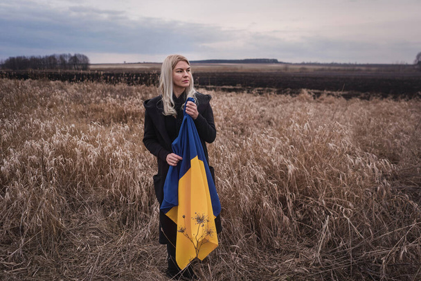 Rusya 'nın Ukrayna' ya karşı savaşı. Yanık bir buğday tarlasında bayrak sallayarak koşan genç, güzel bir vatansever kız. Bağımsız bir ülkenin insanlarının karlı duygusal tablosu, acısı ve umutsuzluğu. - Fotoğraf, Görsel