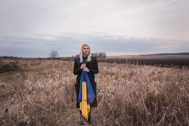 ロシアのウクライナへの戦争。若い、美しい愛国者の女の子が立っている/フラグを持つ焼き小麦のフィールド上で実行しています。独立国家の人々の壮大な感情的な絵、痛みと絶望. - 写真・画像