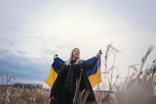 Guerra da Rússia contra a Ucrânia. Jovem, bela menina patriota de pé / correndo em um campo de trigo queimado com uma bandeira. Imagem emocional de grão, dor e desespero do povo de um país independente. - Foto, Imagem