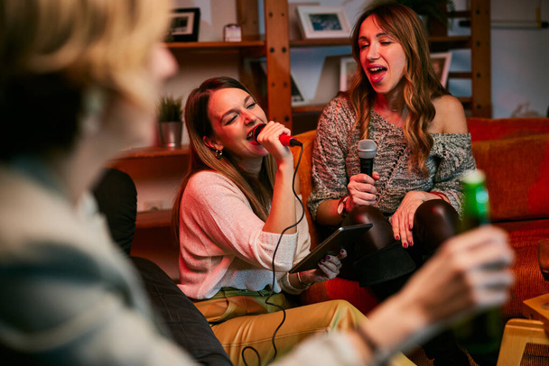 Dziewczyny bawią się w karaoke w domu. - Zdjęcie, obraz