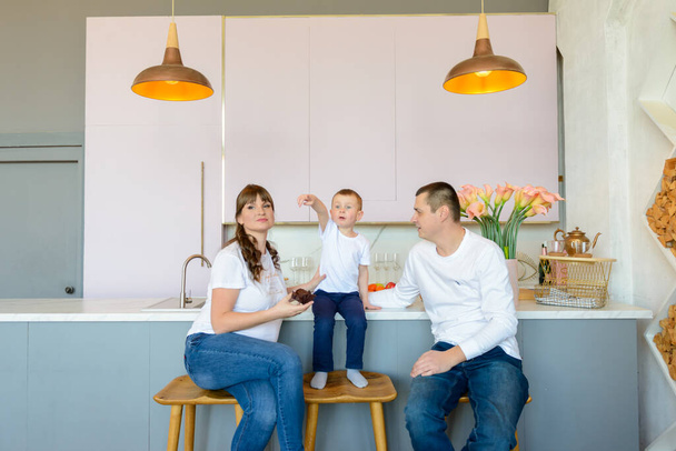 Familia alegre vestida con camisetas blancas divirtiéndose durante su comida en la mesa de comedor. - Foto, imagen
