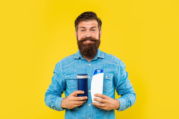 glad brutal bearded man hold hair conditioner bottle on yellow background, haircare - Fotografie, Obrázek