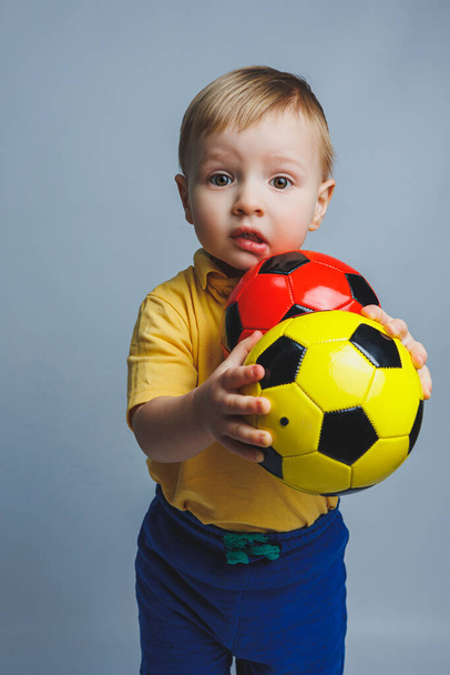Little european boy, fan or player in yellow and blue uniform with a soccer ball, supports the soccer team on a white background. Football sport game, lifestyle concept. Isolated on white background - Фото, зображення
