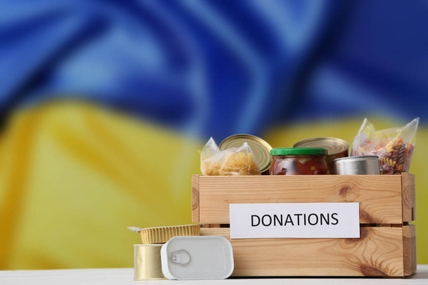 Boîte de don avec des produits contre le drapeau ukrainien. Assistance humanitaire à l'Ukraine - Photo, image