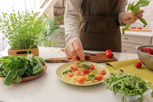 Donna decorare gustosa pasta con basilico a tavola in cucina - Foto, immagini