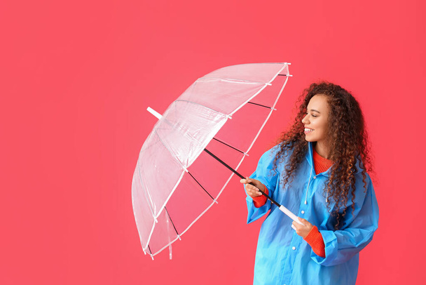 Joven mujer afroamericana en impermeable azul con paraguas sobre fondo rojo - Foto, Imagen