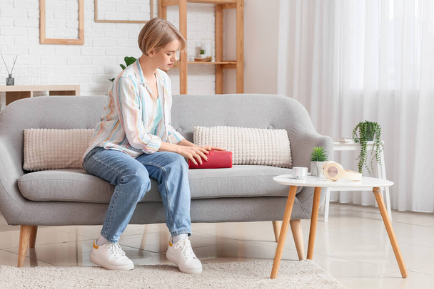Frau mit modernem drahtlosen tragbaren Lautsprecher sitzt auf Sofa im Zimmer - Foto, Bild