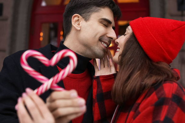 Liefdevol paar met snoep stokken aanraken neuzen op winterdag, close-up - Foto, afbeelding