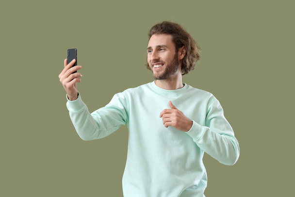 Handsome man with mobile phone taking selfie on green background - Photo, Image