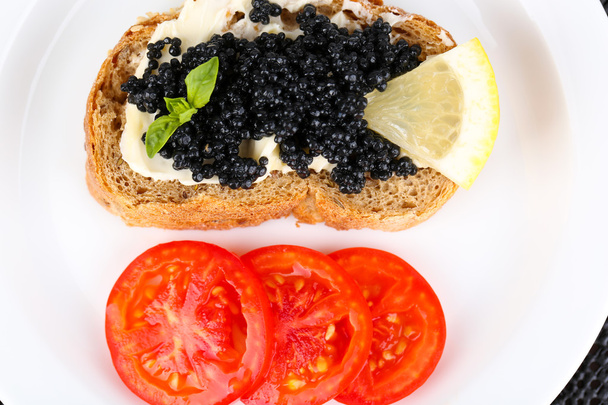 Black caviar and butter on bread with tomatoes on plate closeup - Фото, изображение