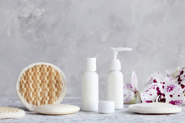 Mock up of body and face cosmetics in different bottles, natural facial sponge, soap and orchid flower. Beauty, spa and cosmetic concept. - 写真・画像