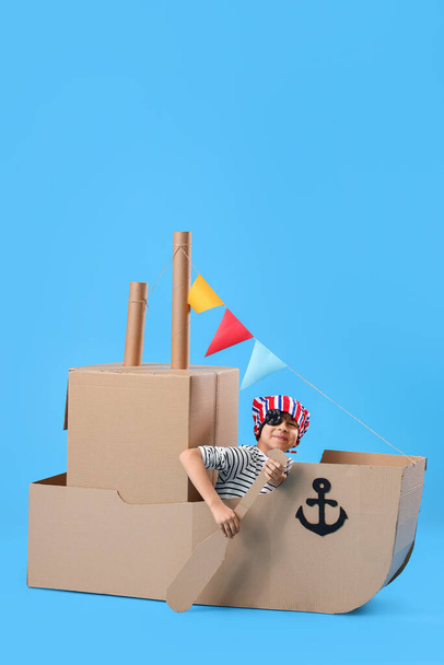 Cute little boy playing with cardboard ship on blue background - Photo, Image