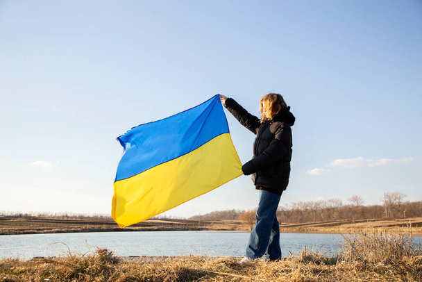 Ukrajinská žlutomodrá vlajka proti obloze v rukou mladé ženy. Národní symbol svobody a nezávislosti. Podpořte Ukrajinu. hrdost a vlastenectví Ukrajinců - Fotografie, Obrázek