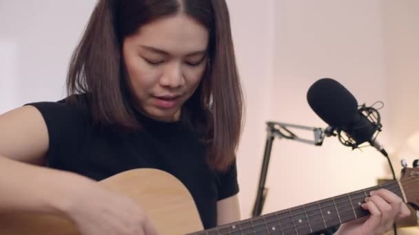 Kaunis aasialainen nainen oppii soittamaan kitaraa ja laulamaan kotona studio. - Materiaali, video