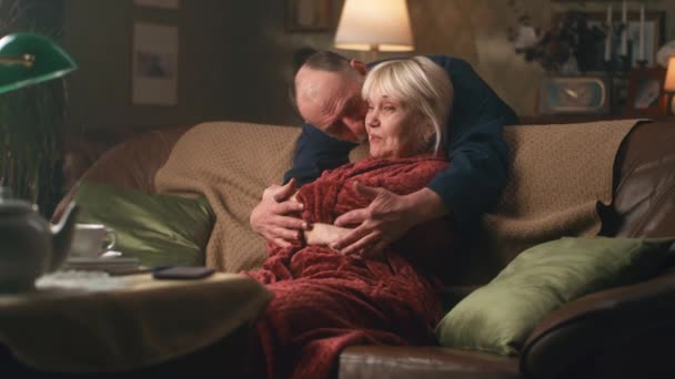 Старший мужчина обнимает удивленную женщину на диване - Кадры, видео
