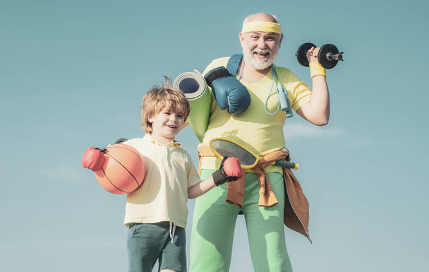 Sports education. Sportsman grandfather and healthy kid with basketball ball on blue sky background. Senior fitness man and son training on blue background. - Foto, Imagem