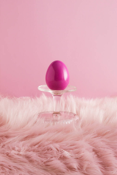 Composizione pasquale fatta di uovo dipinto sul podio e sullo sfondo di pelliccia rosa. Concetto di vacanza minimo. - Foto, immagini