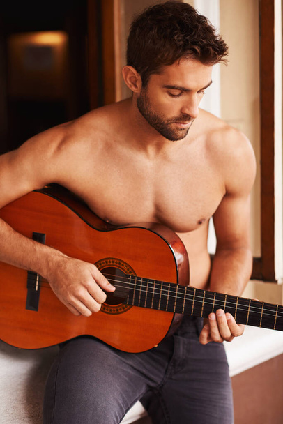 Serenading you with the sweet sounds of his guitar. Cropped shot of a shirtless young man playing guitar at home. - Fotó, kép