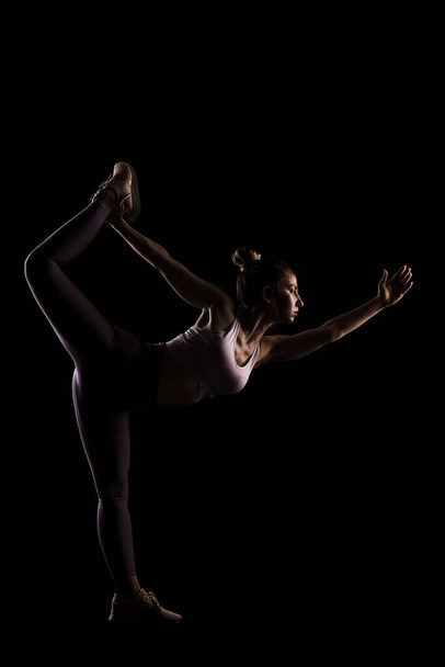 Fit girl practicing yoga in a studio. Half silhouette side lit fitness model - Foto, afbeelding