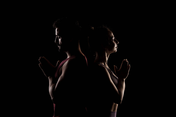 Fit couple posing together. Boy and girl praying back to back side lit silhouettes on black background. - Fotó, kép