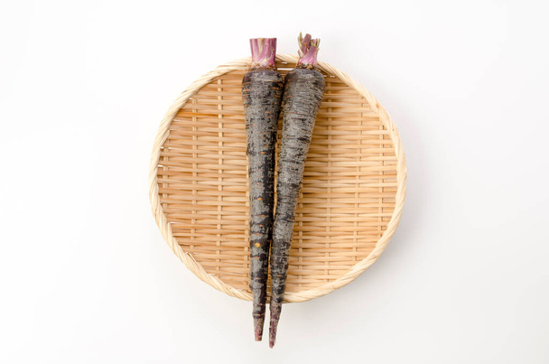Black carrot on bamboo sieve on white background - Photo, Image