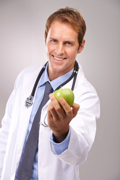 One a day will keep me away. Studio portrait of a handsome young doctor holding out a green apple. - Photo, image