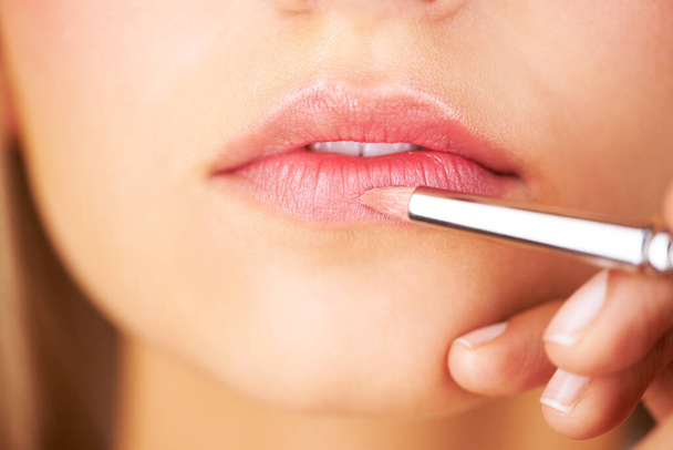 Lippenbekenntnisse. Ausgeschnittene Ansicht einer jungen Frauenlippe, während Lippenstift auf sie aufgetragen wird. - Foto, Bild
