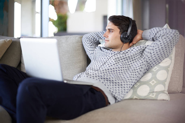 Verloren in de muziek. Opname van een jonge man die naar muziek luistert via zijn laptop. - Foto, afbeelding