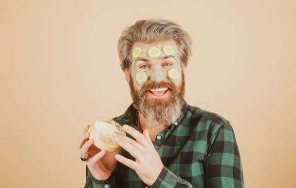 Funny male model with mask and cucumber slices on face. Spa, dermatology, wellness and facial treatment concept. Man having cosmetic moisturizing mask, isolated studio background. Male face care. - Foto, immagini