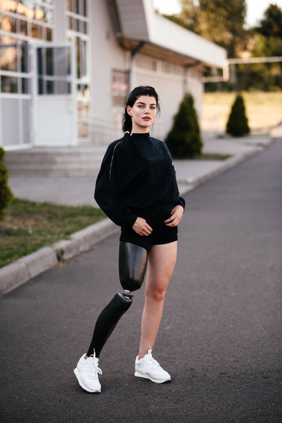 Photo of young athletic disabled girl with prosthetic leg in sportswear walking with smile outdoor - Foto, afbeelding