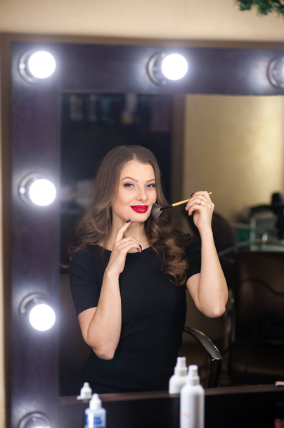 Beautiful girl does makeup and looks in the mirror - 写真・画像