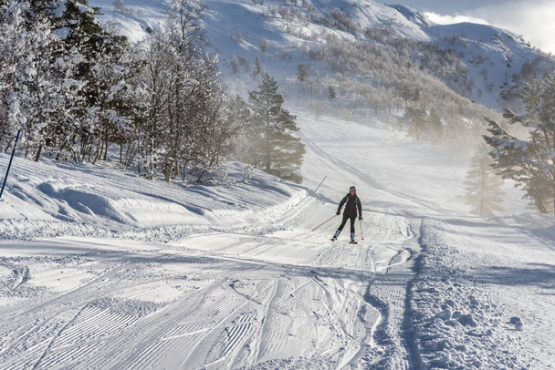 Kobieta z brązowymi włosami uśmiechnięta, ubrana w strój narciarski i plecak zjeżdżająca z trasy ze szczytu góry w ośrodku narciarskim stryn, Norwegia, widok z daleka, poziomy - Zdjęcie, obraz