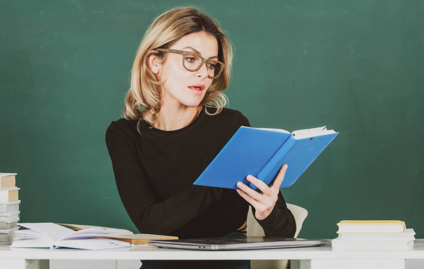 Modern attractive teacher. Portrait of smart young woman in glasses with book on the blackboard in class at high school or collage. Female student study in university. Teachers day. - Φωτογραφία, εικόνα