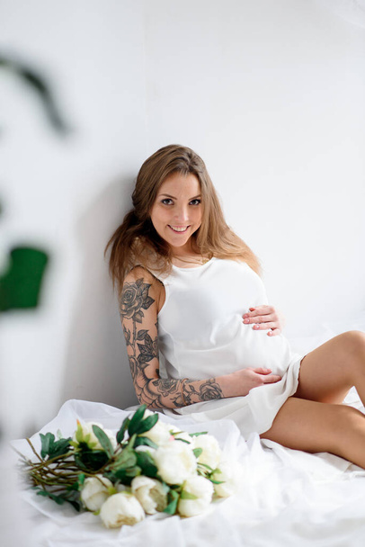 Pregnant girl with tattoo in a white dress. - Fotoğraf, Görsel