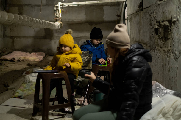 Oroszország háborúja Ukrajnával. Anya és a gyerekek a óvóhelyen ülnek. Tűz Ukrajna békés városaira. Kharkiv bombázása. - Fotó, kép