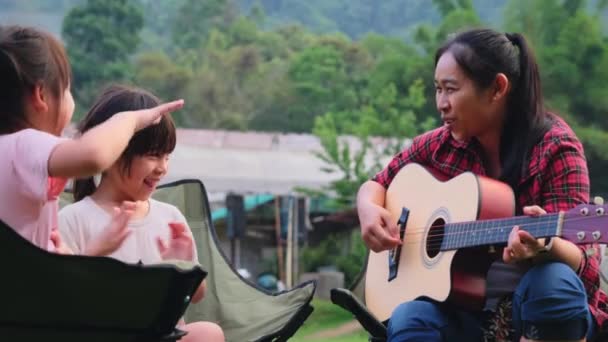 Anne ve çocuk, yaz ormanlarında kamp çadırının yanındaki kamp sandalyelerinde gitar çalıp şarkı söylüyorlar. Aile tatilde birlikte vakit geçirir.. - Video, Çekim