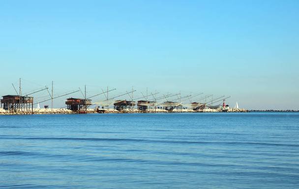 Many fishing huts on the dike and large nets for catching fish and crustaceans in the Adriatic sea in Italy - Photo, Image