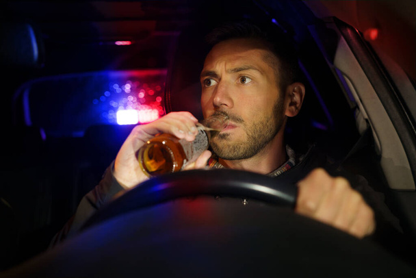 La policía detuvo el coche con conductor borracho dentro. Hombre borracho bebiendo alcohol mientras conducía. Conductor bajo influencia alcohólica - Foto, imagen
