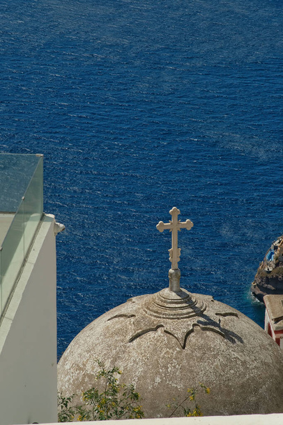 Ein Balkon mit Blick auf die Spitze einer alten Kapelle mit Kruzifix und Ägäis auf Santorin - Foto, Bild