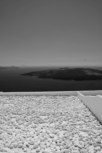  Άποψη του ηφαιστείου της Σαντορίνης από μια ταράτσα γεμάτη πέτρες σε μαύρο και άσπρο - Φωτογραφία, εικόνα