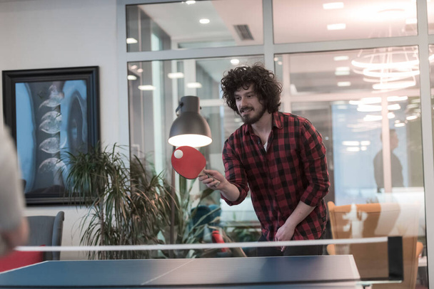 Dois jovens start up homem de negócios jogando ping pong tênis no moderno espaço de escritório criativo grupo de pessoas têm reunião e brainstorming no fundo
 - Foto, Imagem
