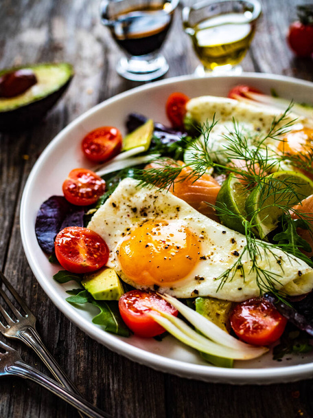 Salmon salad - smoked salmon, sunny side eggs, avocado and fresh vegetables on wooden table  - Foto, Bild