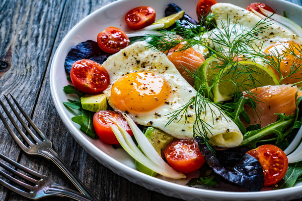 Salmon salad - smoked salmon, sunny side eggs, avocado and fresh vegetables on wooden table  - Foto, immagini