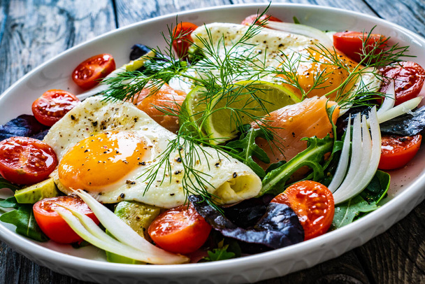 Salmon salad - smoked salmon, sunny side eggs, avocado and fresh vegetables on wooden table  - Photo, image