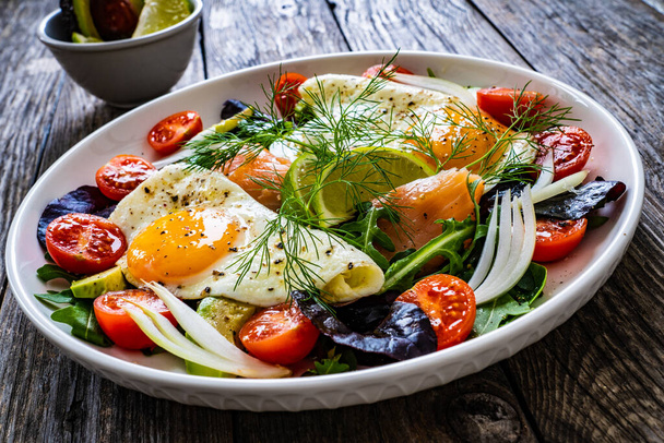 Salmon salad - smoked salmon, sunny side eggs, avocado and fresh vegetables on wooden table  - Fotoğraf, Görsel