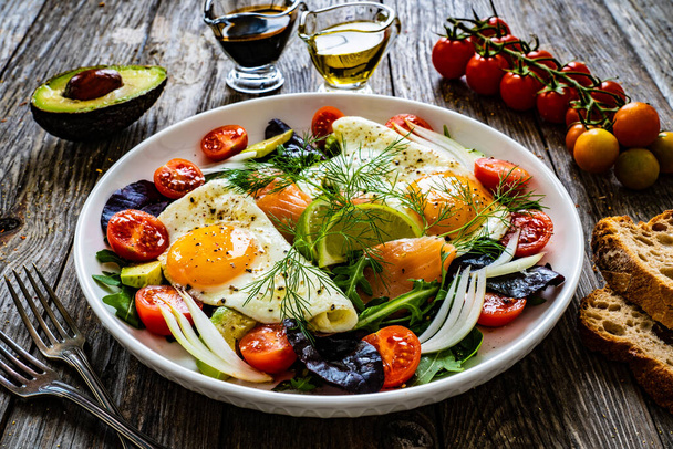 Salmon salad - smoked salmon, sunny side eggs, avocado and fresh vegetables on wooden table  - Φωτογραφία, εικόνα