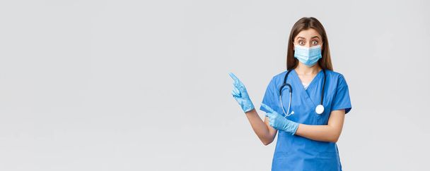 Ковид-19, профилактика вируса, здоровье, медицинские работники и карантин. Заинтересованная и опрошенная женщина-врач, медсестра в синем халате и медицинской маске, задающая вопрос, указывающий налево
 - Фото, изображение